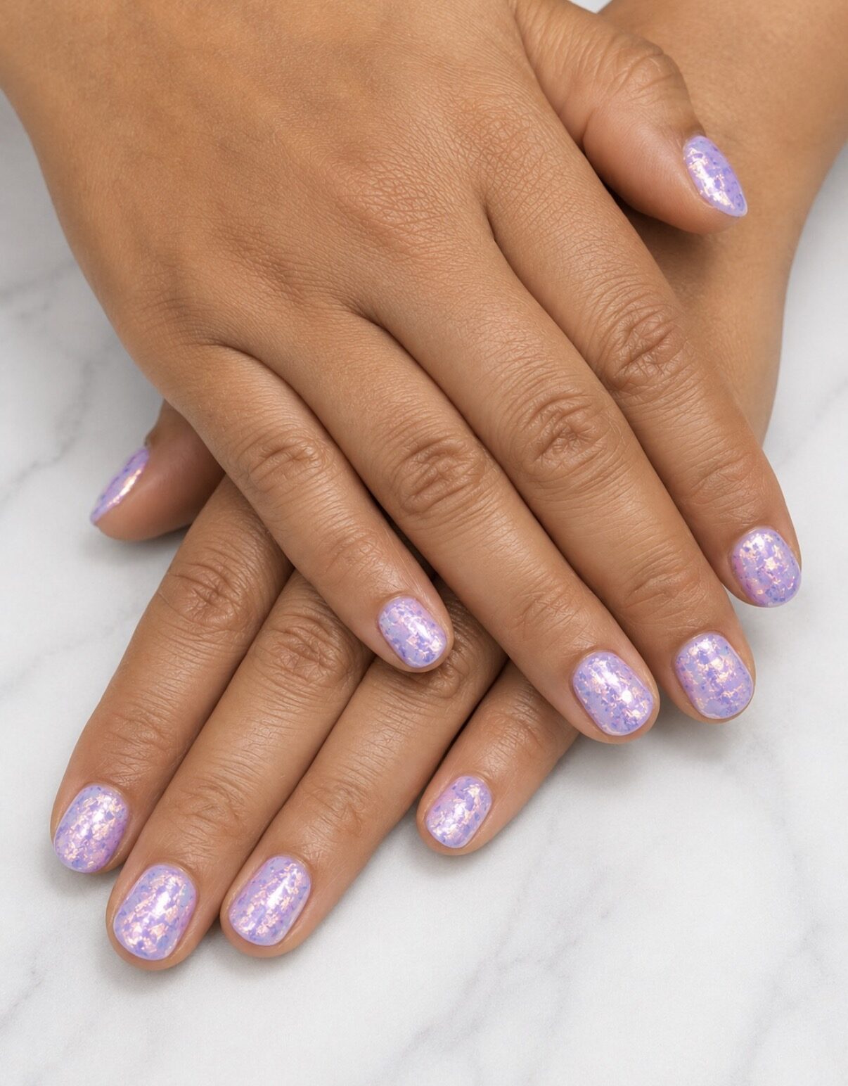 Ongles courts couverts d'un voile irisé lilas à paillettes fines.
