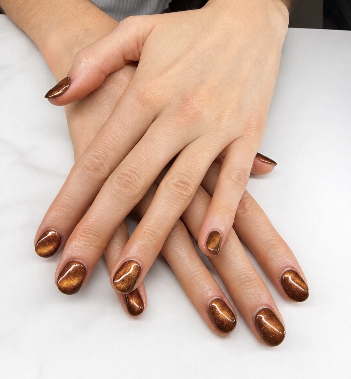 Ongles courts en cat eye cuivré, reflet mobile sous la lumière.