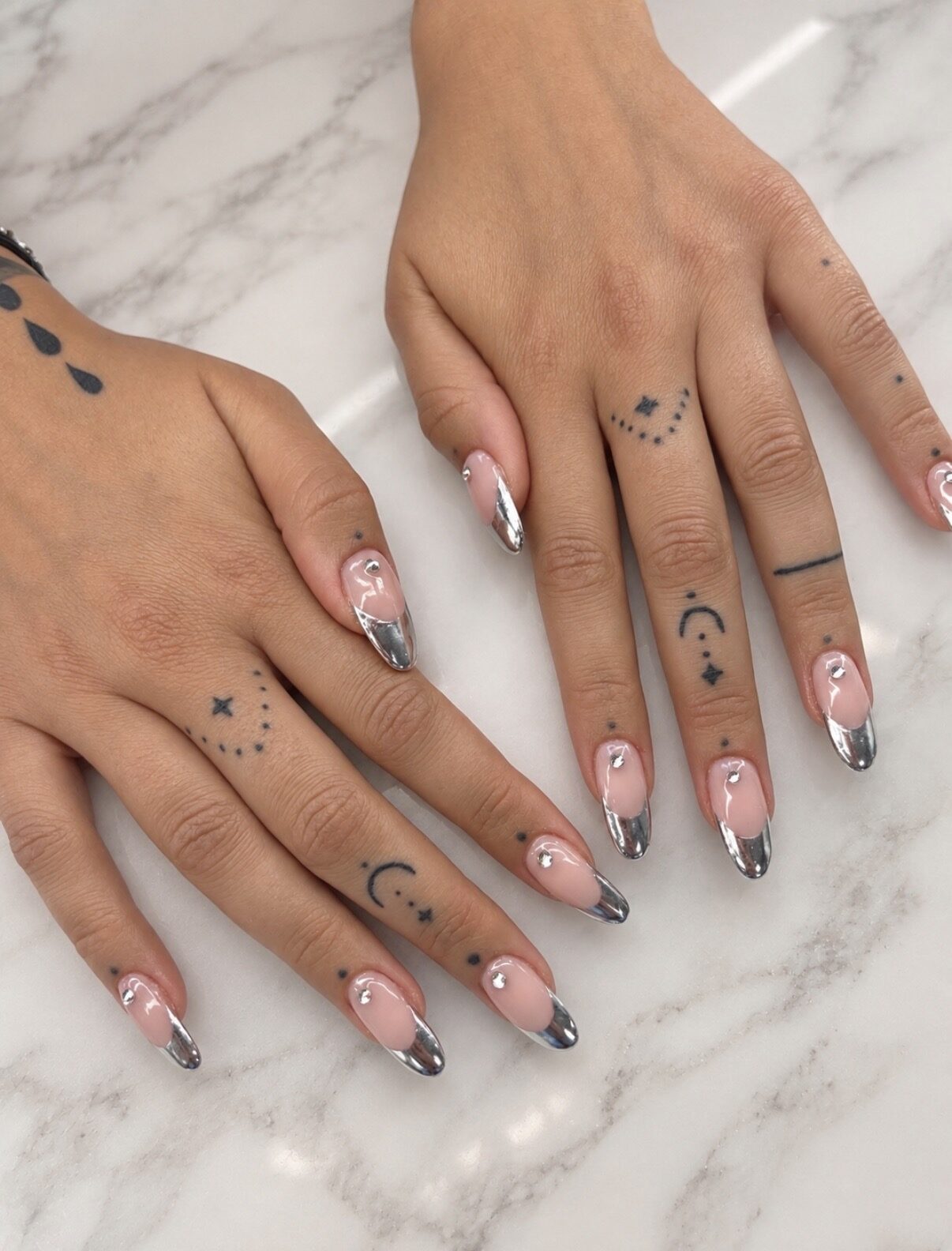 French argentée chromée sur ongles longs, mains tatouées, sur marbre.