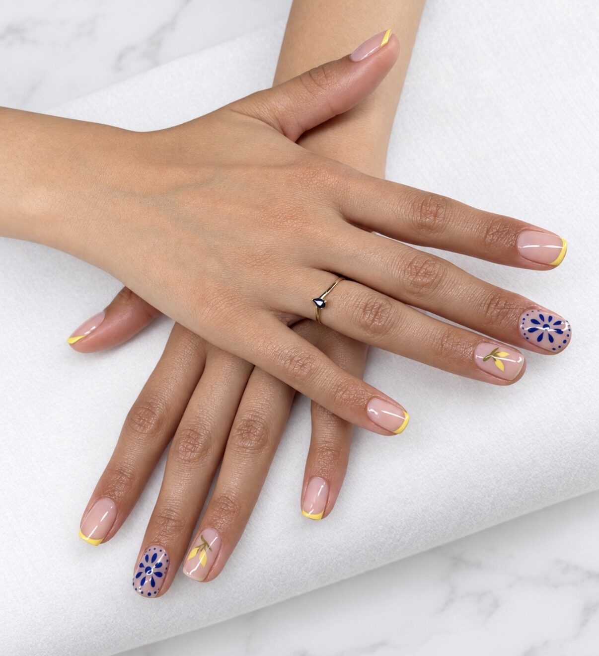 Nail art : French jaune et fleurs bleues peintes à la main sur deux ongles.