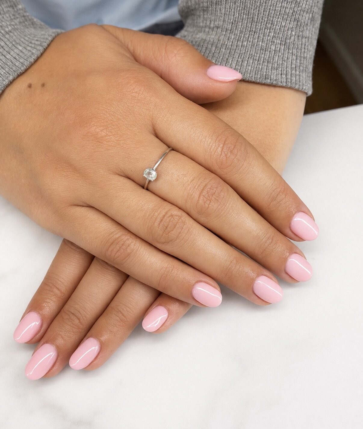 Ongles amande rose pâle laiteux, finition brillante, sur un plan de marbre blanc.